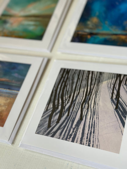 A close-up of several art card prints arranged in a grid, with one print in sharp focus showing dark tree-like strokes over a pale background. The surrounding prints are blurred, and no person or real environment is visible beyond a neutral surface.