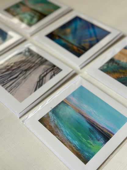 A set of art print cards arranged on a light surface, showing abstract landscape and seascape paintings with white borders and varying color palettes.