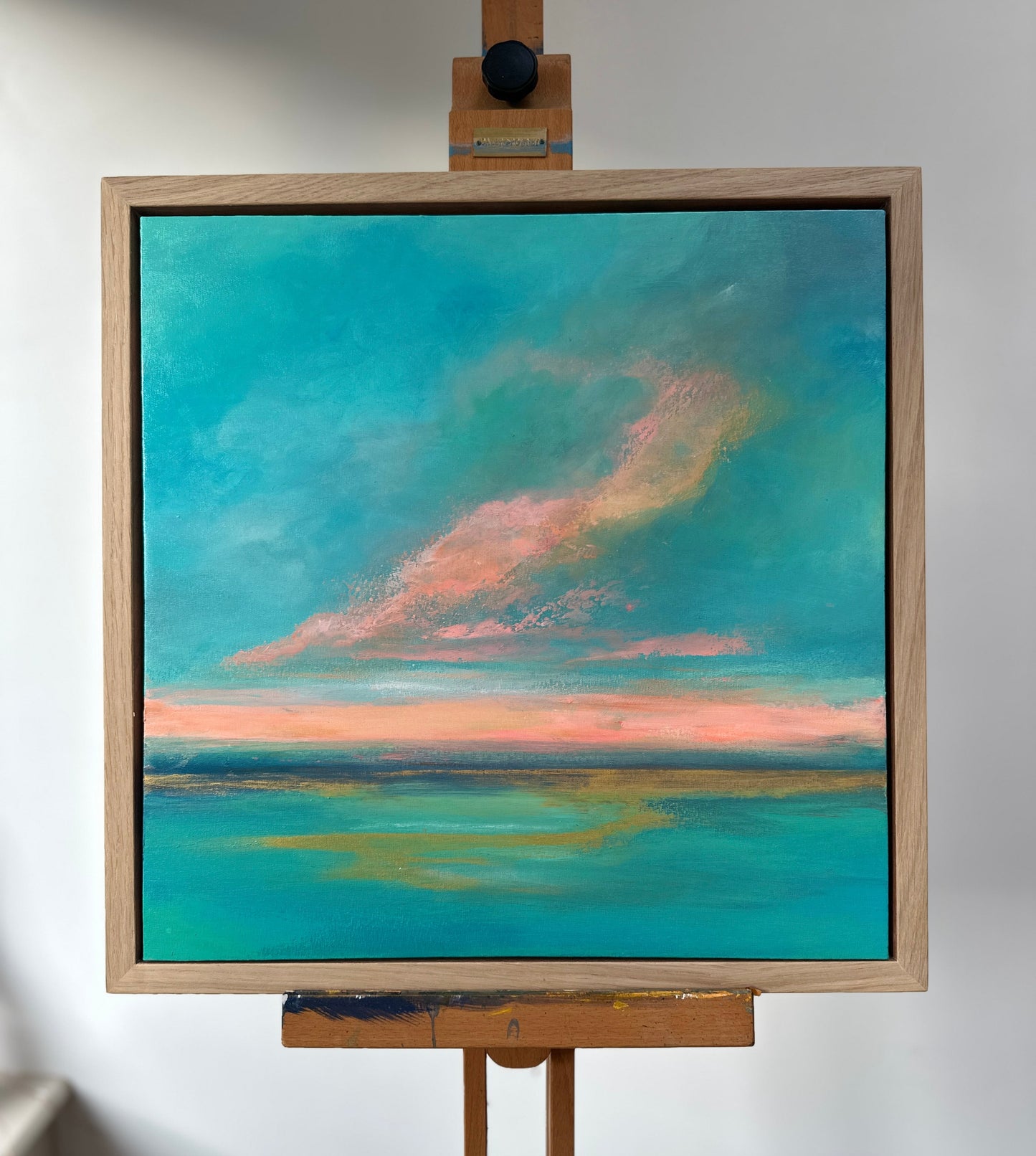 Painting of a landscape with a blue sky and pink clouds on an easel.