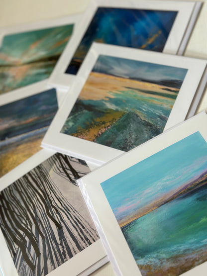 A set of framed landscape art prints fanned out on a light surface. The prints feature textured, impressionistic landscapes in teal, blue, green, gold, and black-and-white tree patterns.