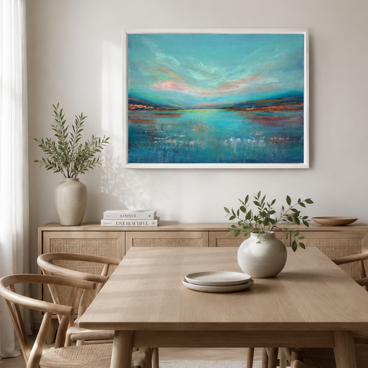 A framed abstract landscape painting with turquoise, blue, and copper tones hangs on a light beige wall above a wooden dining table and chairs in a styled interior room.